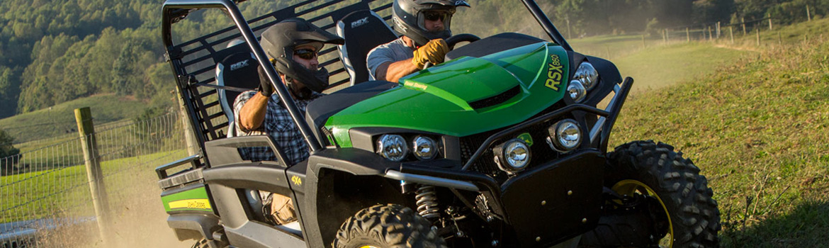Two people riding in a John Deere UTV down a dirt road that's next to a wire fence